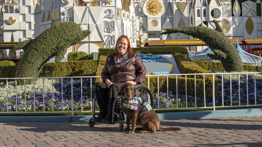Erin Quintanilla in front of "it's a small world" with her service dog