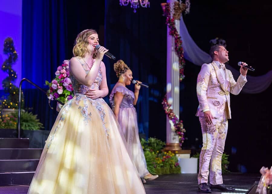 Wish kid Mikayla sings onstage with two other Disney performers in yellow ball gown.