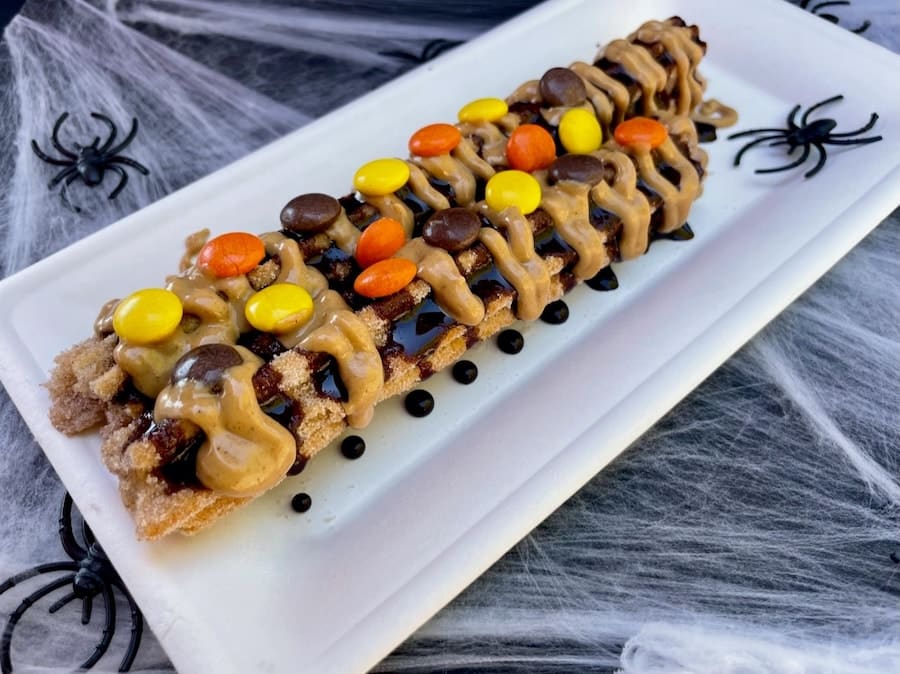 | The Main Street Mouse in Honor of Halfway to Halloween Guests Can Visit the Downtown Disney District and Try a Spooky Churro Rolled in Cinnamon Sugar Cut in Half Drizzled with Peanut Butter and Chocolate Sauce and Topped with Orange Yellow and Brown Peanut Butter Candy Pieces from April 28 Through May 1 2022