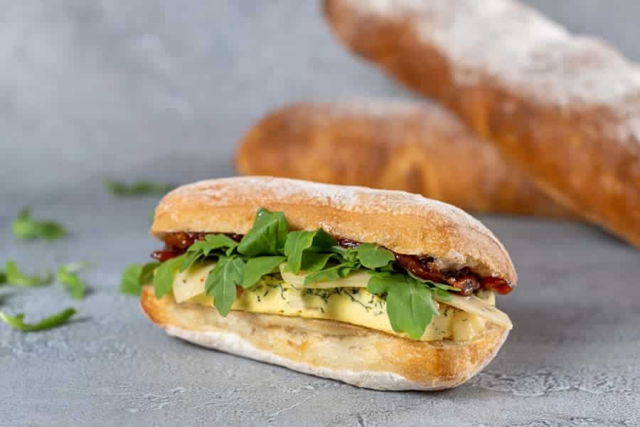 Plant-based Ciabatta Sandwich with “egg” Florentine, plant-based cheese, tomato jam, and arugula.