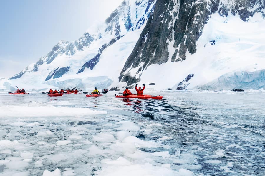 People kayaking in icy water with snow covered mountains in the background