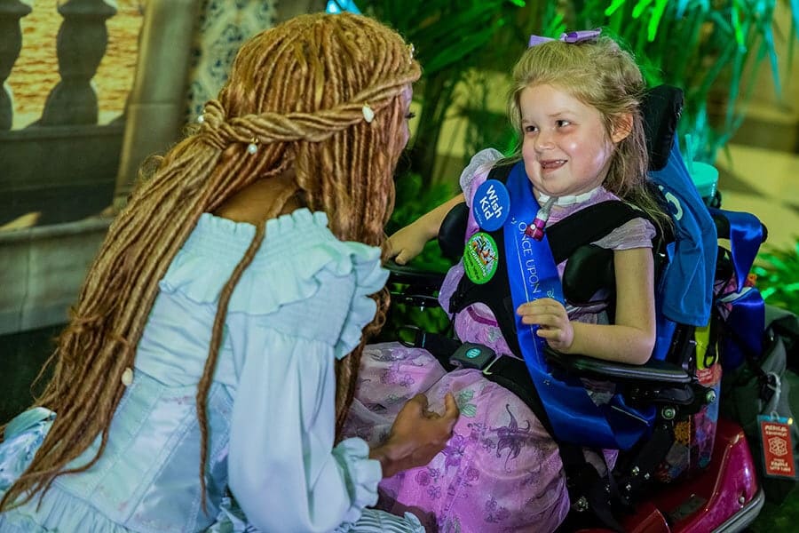 Young female wish child in a wheelchair smiles at live action Ariel