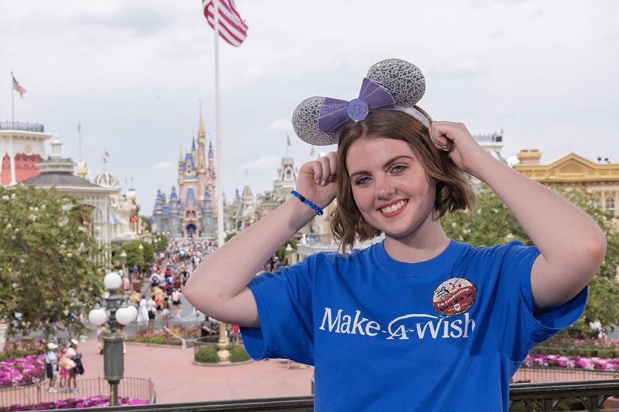 Female wish kid wearing Mickey ears poses at Magic Kingdom. 