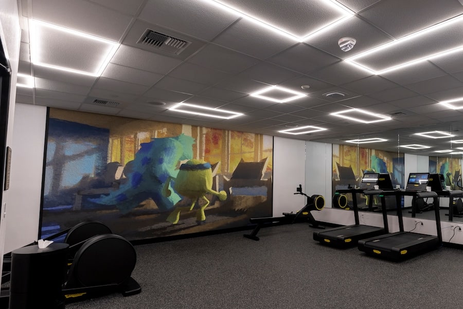 Pixar Place Hotel gym (fitness center) with mural of Mike and Sulley running on a treadmill, inspired by Pixar’s “Monsters University”