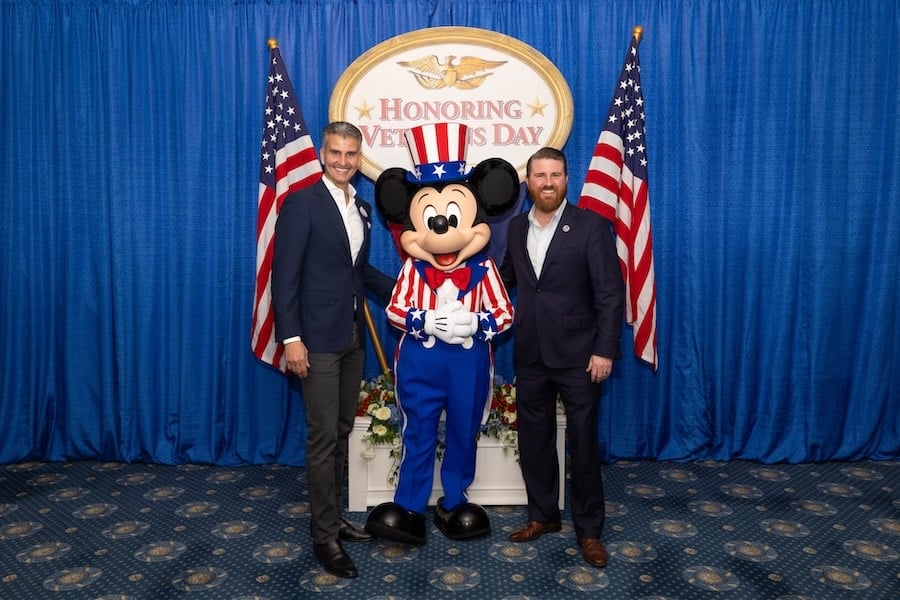 Photo of Josh DAmaro Chairman of Disney Experiences with Jared Lyon president and CEO of Student Veterans of America with Patriotic Mickey Mouse and a sign that says Honoring Veterans Day