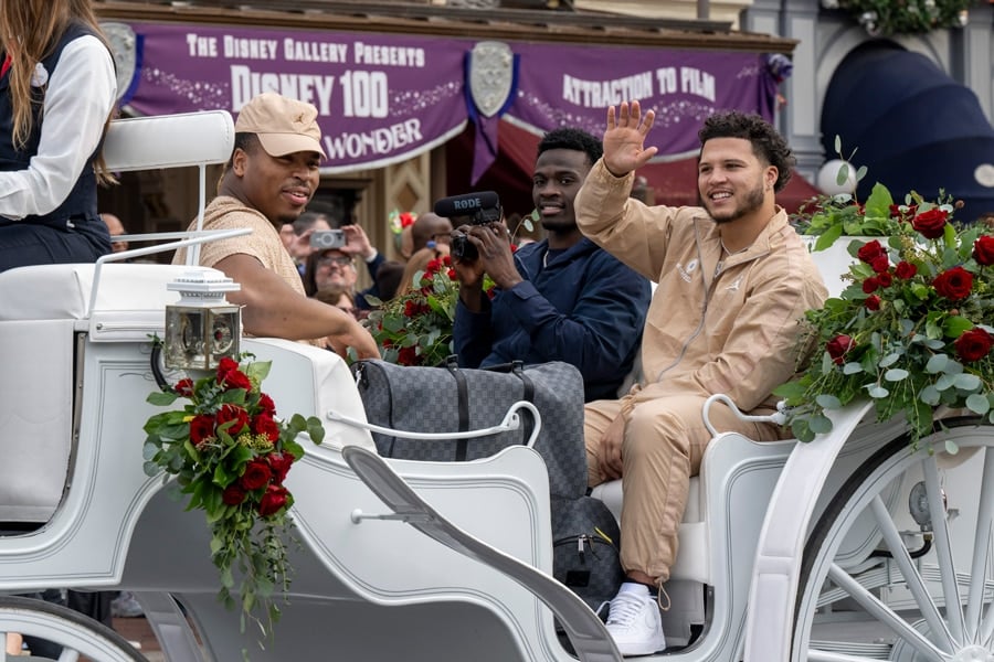 Michigan Head Coach Jim Harbaugh and Michigan players: defensive back Mike Sainristil, defensive lineman Kris Jenkins, and running back Blake Corum riding down Main Street USA at Disneyland