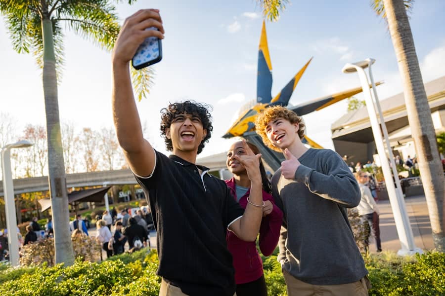 Image of Percy Jackson and the Olympians cast Walker Scobell (Percy), Leah Jeffries (Annabeth) and Aryan Simhadri (Grover Underwood) posing for a selfie in front of Guardians of the Galaxy: Cosmic Rewind
