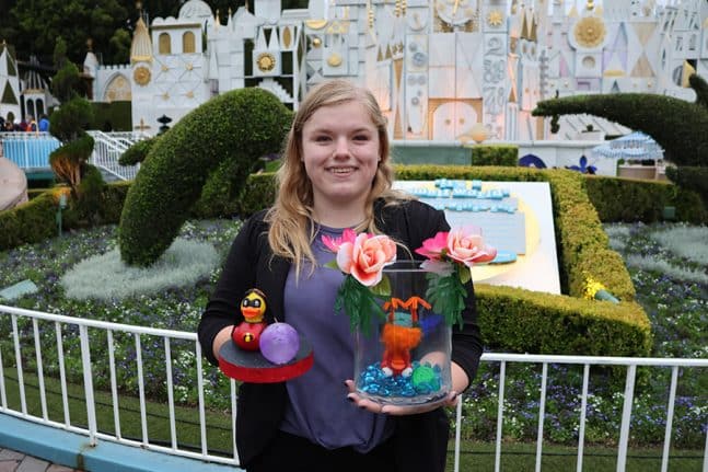 | The Main Street Mouse a Cast Member Poses in Front of it's a small world" with two of her rubber duck designs