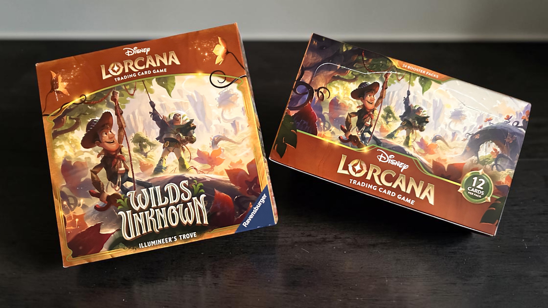 Two Disney Lorcana trading card game boxes sit on a dark wooden surface with colorful fantasy artwork and character illustrations visible on both boxes The left box reads Wilds Unknown Illumineers Trove The right box shows a 12 Cards per Pack badge and Lorcana branding
