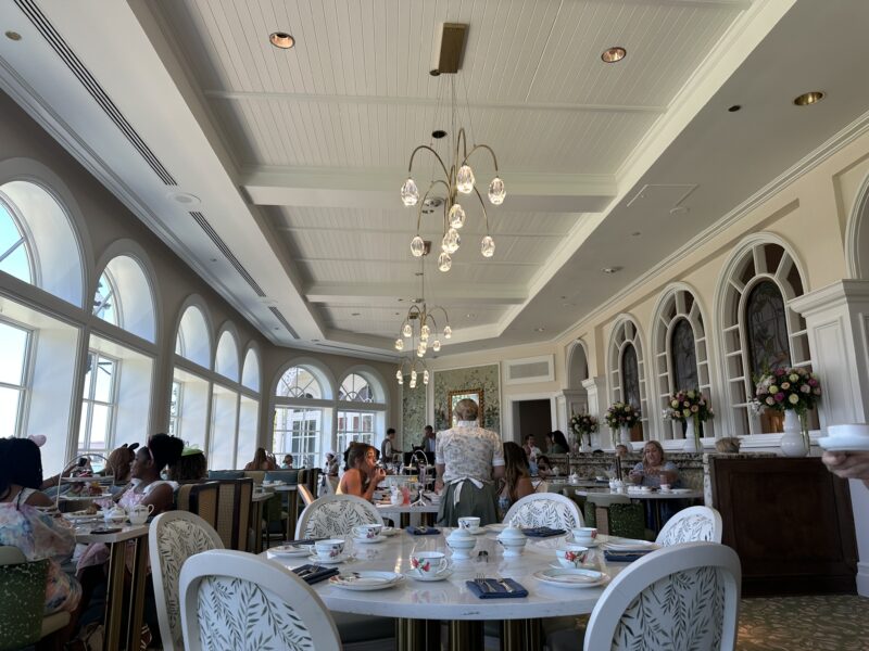 Elegant dining room with arched windows white paneled ceiling crystal chandeliers and guests enjoying tea and desserts at tables