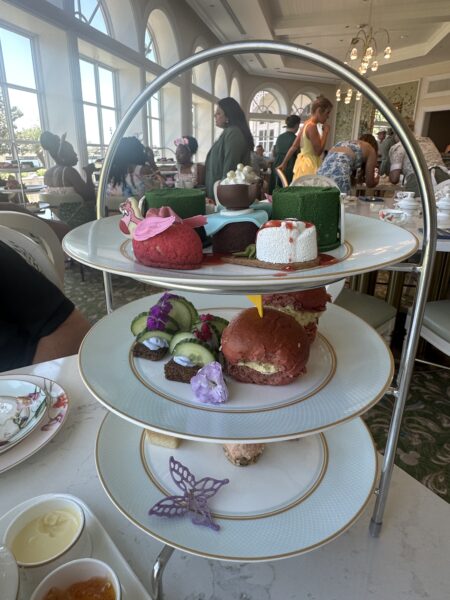 Three tiered serving stand with assorted pastries at a sunlit tea room guests mingling in the background
