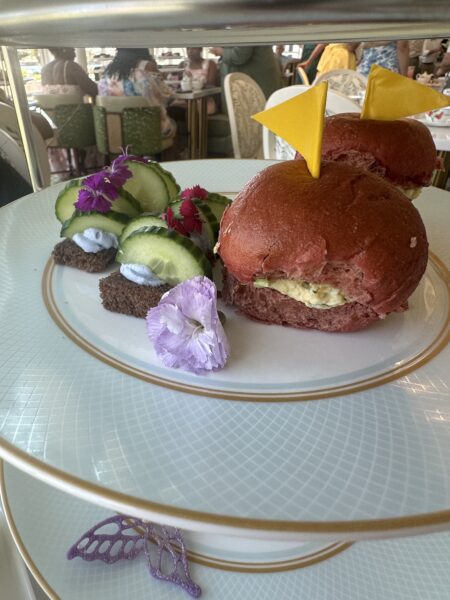 Plate of dessert with red cream filled buns and cream filling topped with yellow flag shapes beside cucumber ribbons and edible flowers on a decorative plate
