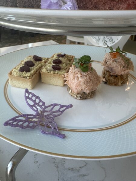 Plate of appetizers two olive topped crackers and two pink tuna croστini with herbs on a decorative plate with a purple butterfly ornament