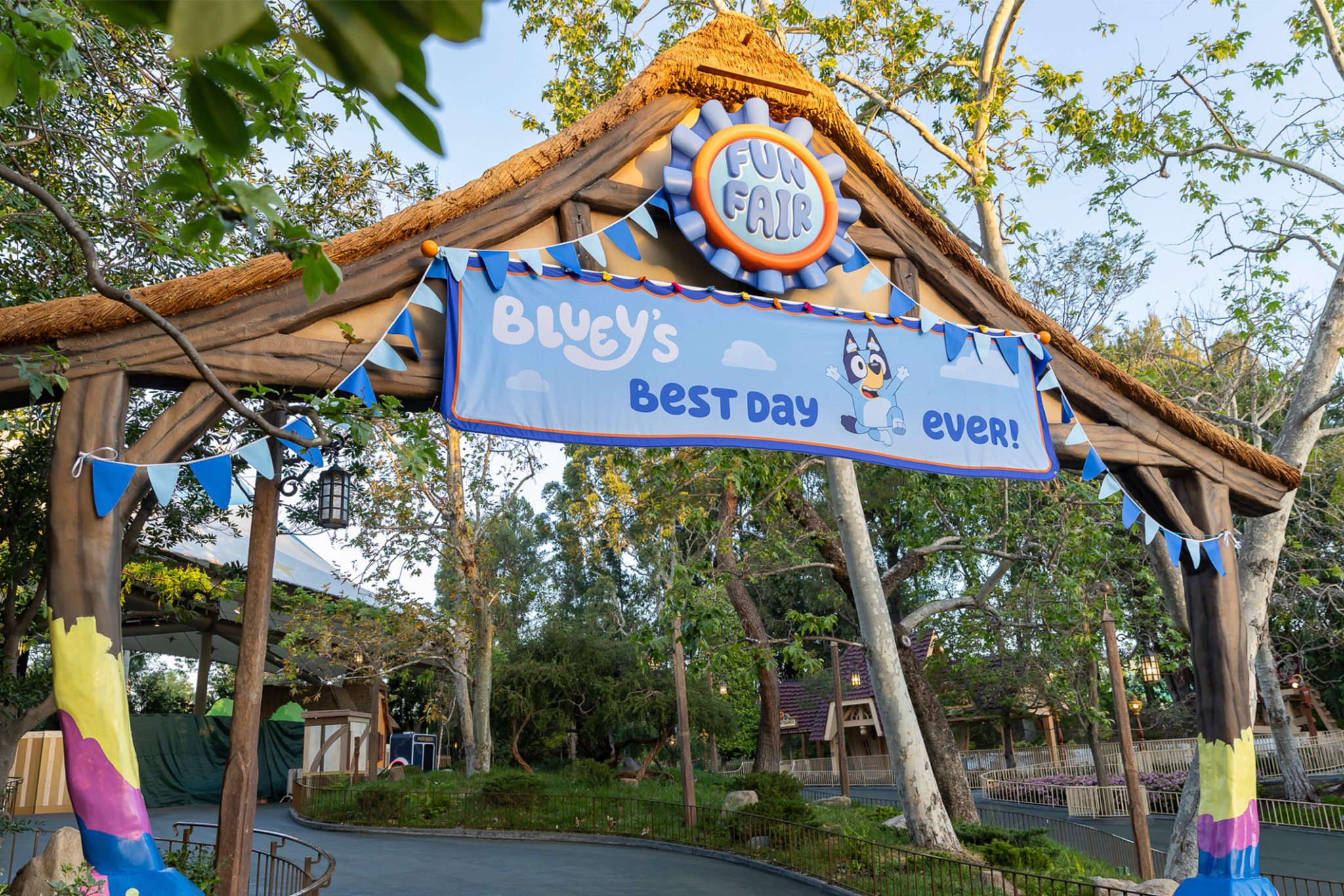 031126CT95932048x1366 | The Main Street Mouse Entrance to a Fun Fair with a Blue Banner Reading blueys Best Day Ever Under a Thatched Roof