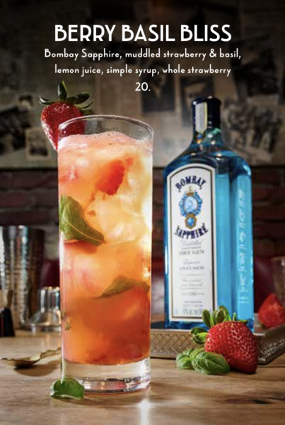 Tall Berry Cocktail with a Strawberry Garnish and Mint Alongside a Bombay Sapphire Gin Bottle on a Bar