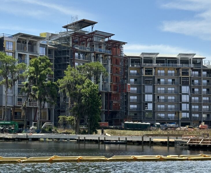 Under construction multi story apartment building along a river with scaffolding and exposed framework against a blue sky