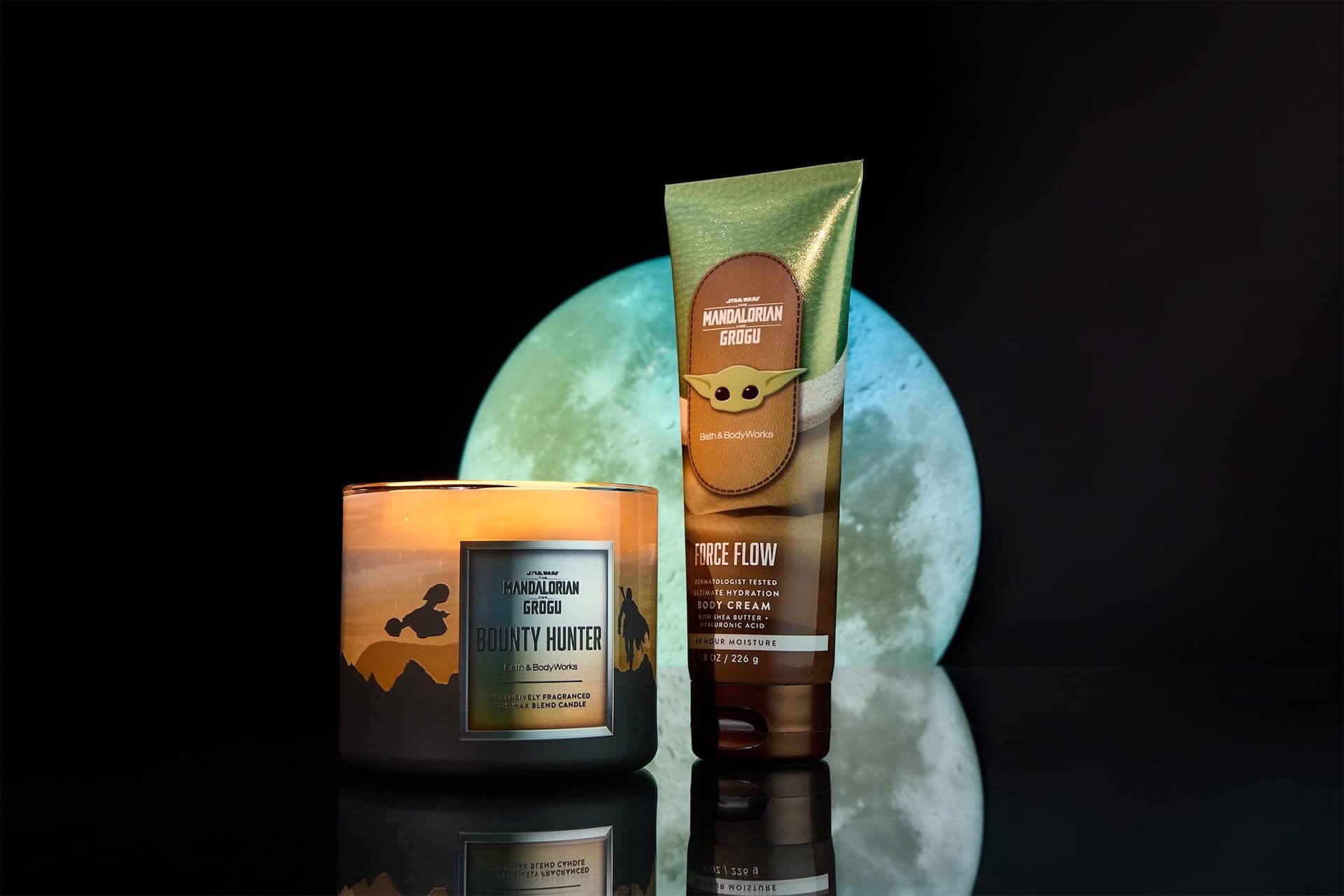 Product shot of Star Wars Mandalorian care items a Grogu themed lotion tube and a Bounty Hunter candle against a dark background with a pale blue moon prop behind