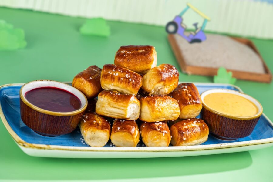 Pile of Glossy Pretzel Bites Stacked on a Blue Tray with Two Dipping Sauces red and Yellow on the Side