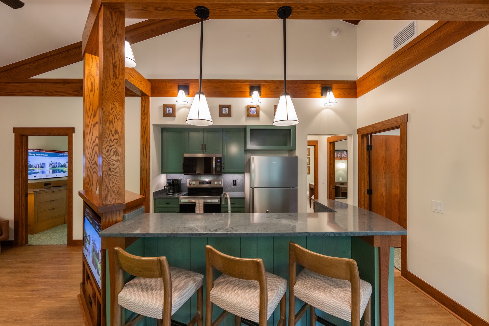2026DVCReimaginedTreehouseVillas14 | The Main Street Mouse Kitchen with Teal green Cabinets Stainless Steel Appliances and a Marble Island Under Three Pendant Lights in a Wood beamed Room Capable of Hosting Bar Seating with Four Chairs Nearby