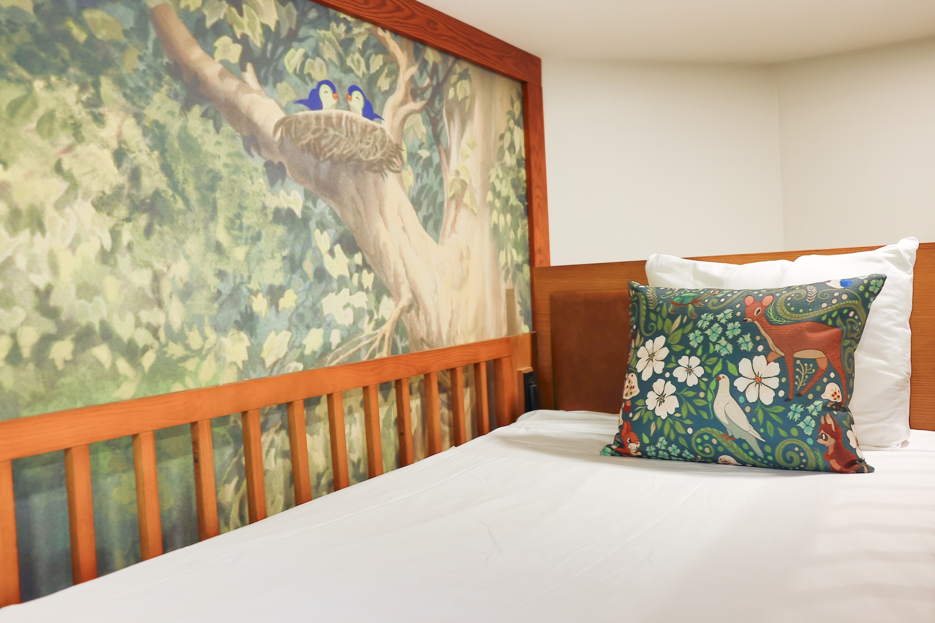 2026DVCReimaginedTreehouseVillas19 | The Main Street Mouse Bedroom with a Mural of Two Blue Birds Perched in a Tree Above a Wooden Headboard White Sheets and Decorative Pillows