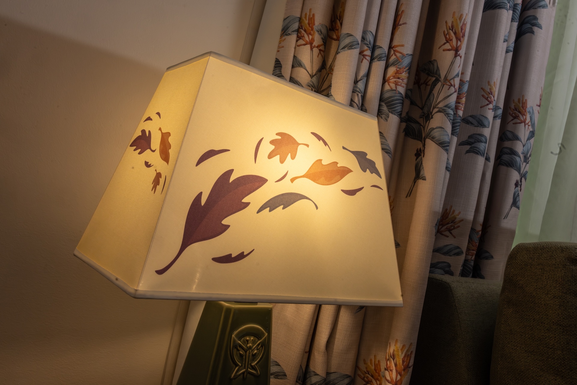 2026DVCReimaginedTreehouseVillas21 | The Main Street Mouse Angled Beige Lampshade with a Leaf Pattern Casting Warm Light Beside Botanical Curtains in a Living Room
