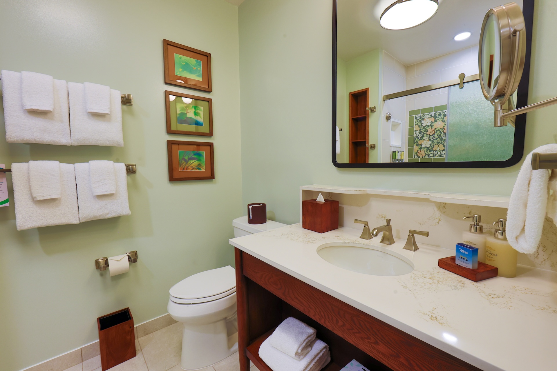 2026DVCReimaginedTreehouseVillas9 | The Main Street Mouse Mint Bathroom with a Double sink Vanity Large Mirror White Towels on Metal Racks and Tropical framed Art on the Wall